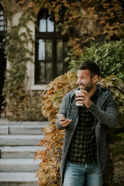 Snygg Ung Man Som Använder Mobiltelefon Och Håller Hämtkaffe Parken — Stockfoto