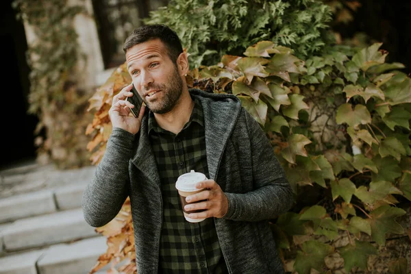 Przystojny Młodzieniec Korzystający Telefonu Komórkowego Trzymający Kawę Wynos Parku — Zdjęcie stockowe