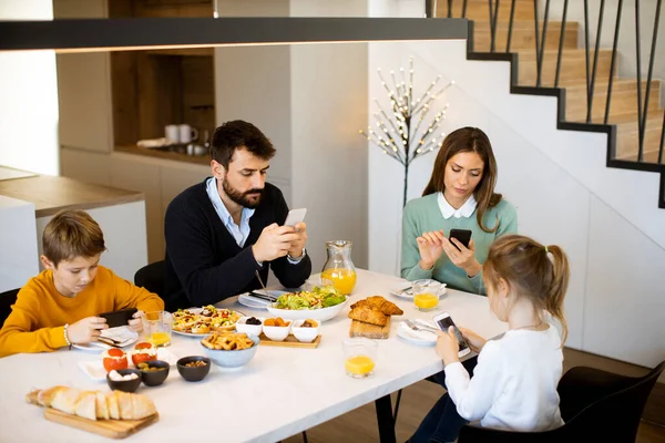 Family using mobile phones while having breakfast at dining table at the apartment