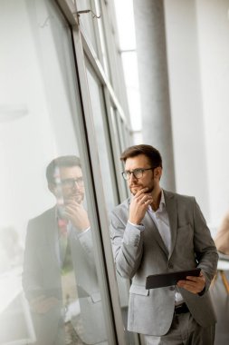 Ofis penceresinin yanında dijital tabletle duran yakışıklı genç işadamı