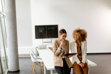 Dijital tablet tutan ve modern ofiste çalışan iki genç kadın.