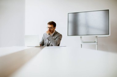 Bilgisayarda çalışan yakışıklı genç adam parlak ofiste arkasında büyük ekranla.