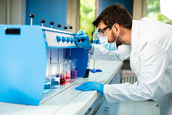 Young researcher with protective goggles checking test tubes in flocculator at the laboratory