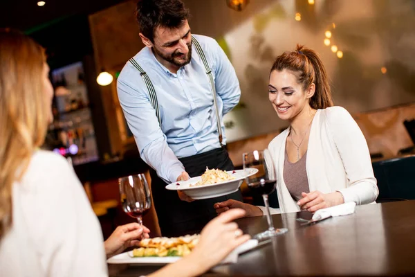 Przystojny Młody Kelner Serwujący Jedzenie Kobietom Restauracji — Zdjęcie stockowe