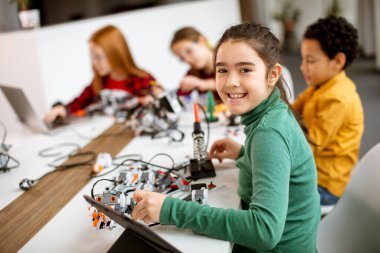 Robot sınıfında elektrikli oyuncak ve robot programlayan bir grup mutlu çocuk.