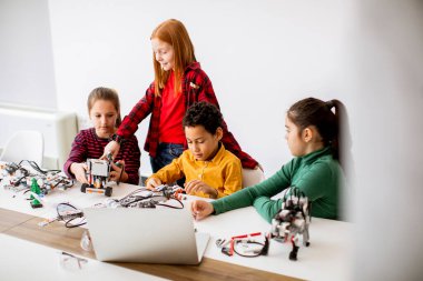 Robot sınıfında elektrikli oyuncak ve robot programlayan bir grup mutlu çocuk.
