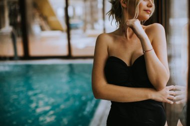 Kapalı yüzme havuzunun penceresinin yanında duran güzel genç bir kadın.