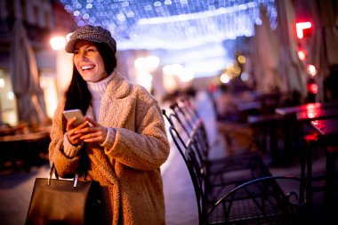 Noel zamanı sokakta cep telefonunu kullanan güzel genç bir kadın.