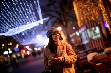 Noel zamanı sokakta cep telefonunu kullanan güzel genç bir kadın.