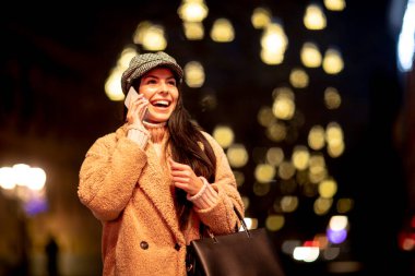 Noel zamanı sokakta cep telefonunu kullanan güzel genç bir kadın.