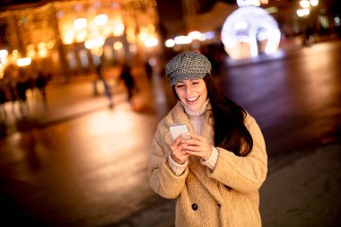 Noel zamanı sokakta cep telefonunu kullanan güzel genç bir kadın.