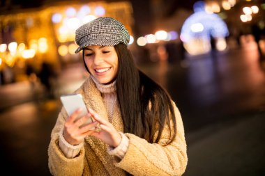 Noel zamanı sokakta cep telefonunu kullanan güzel genç bir kadın.