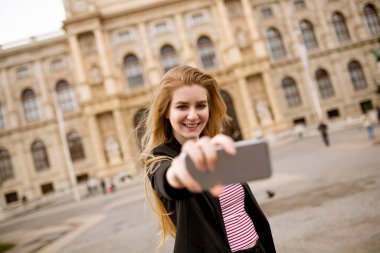 Avusturya, Viyana 'nın merkezindeki sokakta cep telefonuyla selfie çeken genç bir bayan turist.