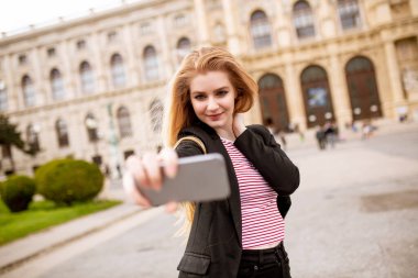 Avusturya, Viyana 'nın merkezindeki sokakta cep telefonuyla selfie çeken genç bir bayan turist.