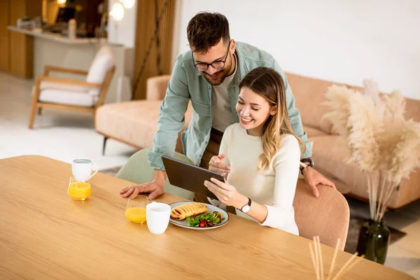 デジタルタブレットを使用して素敵な若いカップルとキッチンで朝食を持っています — ストック写真