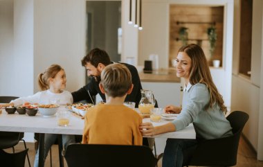 Genç mutlu aile, evdeki yemek masasında kahvaltı ederken konuşuyor.