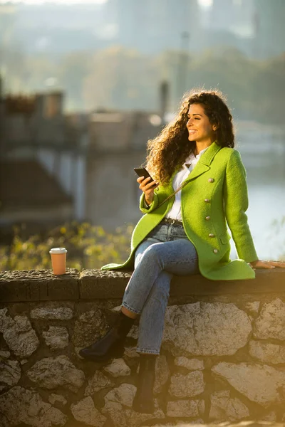 Όμορφη Νεαρή Σγουρή Γυναίκα Μαλλιά Χρησιμοποιώντας Smartphone Ενώ Κάθεται Δίπλα — Φωτογραφία Αρχείου