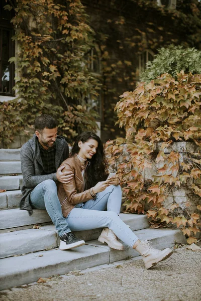 秋天的一天 一对年轻貌美的夫妇坐在室外楼梯上 用手机 — 图库照片