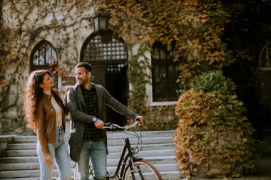 Güz parkında bisikletle yürüyen yakışıklı genç çift.