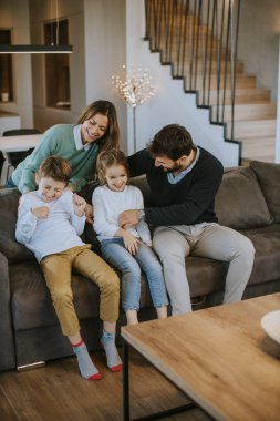 İki çocuklu mutlu bir aile. Oturma odasındaki kanepede birlikte eğleniyorlar.