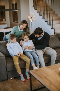İki çocuklu mutlu bir aile. Oturma odasındaki kanepede birlikte eğleniyorlar.