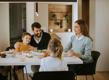 Evdeki yemek masasında yemek yerken genç mutlu aile sohbeti.