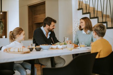 Genç mutlu aile, evdeki yemek masasında kahvaltı ederken konuşuyor.