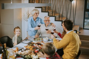 Mutlu bir aile evde kırmızı şarapla yemek yiyor.