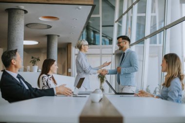 Olgun bir iş kadını ofiste genç bir meslektaşla tokalaşıyor.
