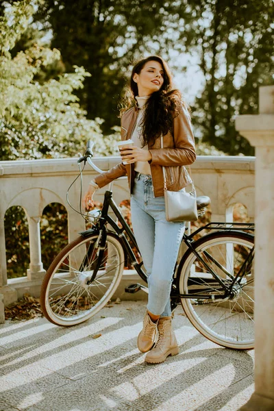 秋の日に自転車でテイクアウトコーヒーカップを持っているかなり若い女性 — ストック写真