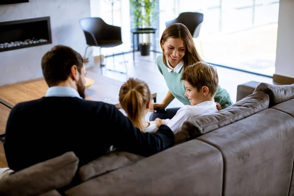 Oturma odasındaki kanepede birlikte televizyon izleyen gülümseyen genç aile.