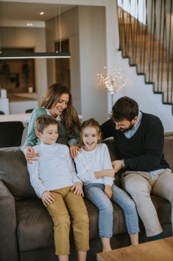 İki çocuklu mutlu bir aile. Oturma odasındaki kanepede birlikte eğleniyorlar.