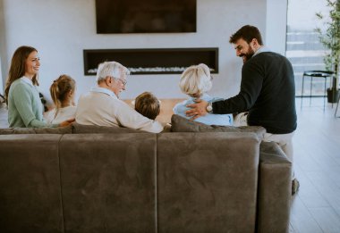 Modern dairenin kanepesinde oturup televizyon izleyen çok nesilli bir aile.