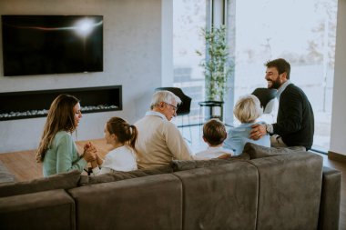 Modern dairenin kanepesinde oturup televizyon izleyen çok nesilli bir aile.