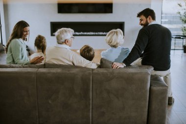 Modern dairenin kanepesinde oturup televizyon izleyen çok nesilli bir aile.