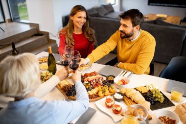 Mutlu bir aile evde kırmızı şarapla yemek yiyor.