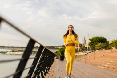 Nehir kenarındaki iskelede egzersiz yapan güzel genç bir kadın.