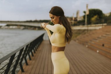 Nehir kenarındaki iskelede esneme egzersizi yapan güzel genç bir kadın.