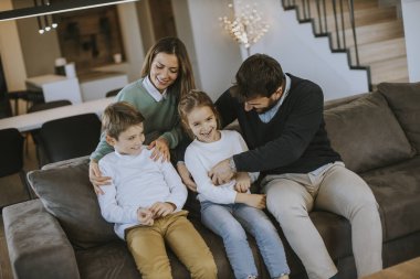 İki çocuklu mutlu bir aile. Oturma odasındaki kanepede birlikte eğleniyorlar.