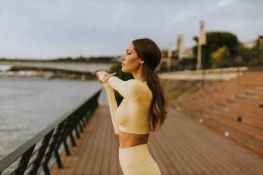 Nehir kenarındaki iskelede esneme egzersizi yapan güzel genç bir kadın.