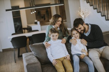 İki çocuklu mutlu bir aile. Oturma odasındaki kanepede birlikte eğleniyorlar.