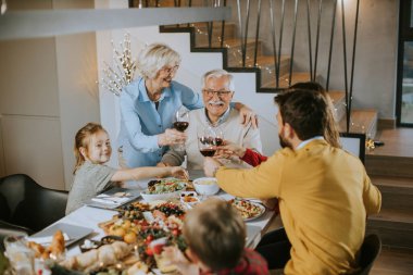 Mutlu bir aile evde kırmızı şarapla yemek yiyor.