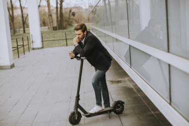 Ofis binasının yanında sokakta elektrikli scooter kullanan yakışıklı genç bir iş adamı.