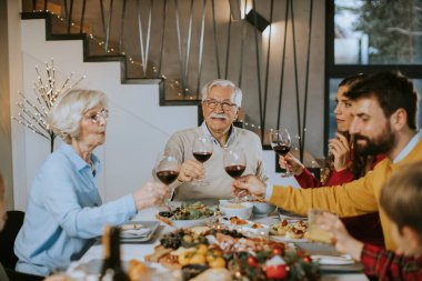 Mutlu bir aile evde kırmızı şarapla yemek yiyor.