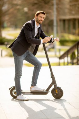 Elektrikli scooter 'da cep telefonu kullanan yakışıklı genç işadamı.