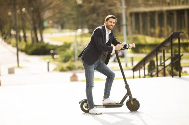 Elektrikli scooter 'da cep telefonu kullanan yakışıklı genç işadamı.