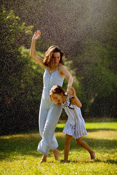 可愛いです女の子持っています楽しいです水とともに灌漑スプリンクラーとともに彼女の母親 — ストック写真
