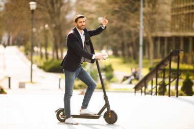 Elektrikli scooter 'da cep telefonu kullanan yakışıklı genç işadamı.