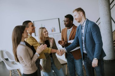 Genç yaratıcı ekip üyeleri modern ofiste çalışırken el sıkışıyor.