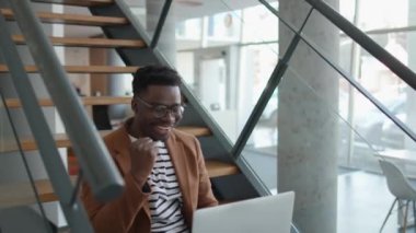 Ofis merdivenlerinde otururken dizüstü bilgisayarda çalışan yakışıklı, Afro-Amerikan iş adamı.